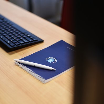 Синий фирменный блокнот DL Academy с белой ручкой.
